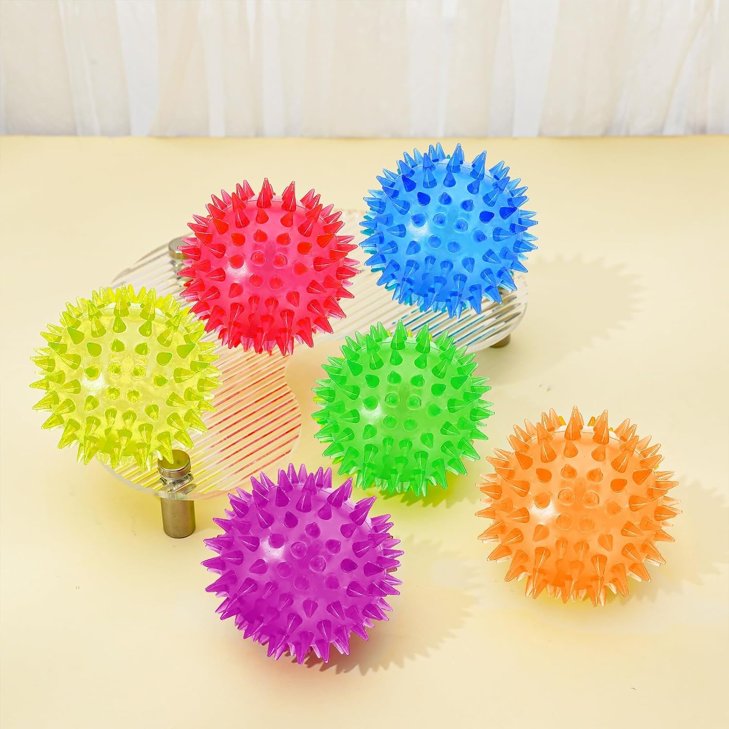 Colorful spiky balls on a wooden surface with a white curtain background