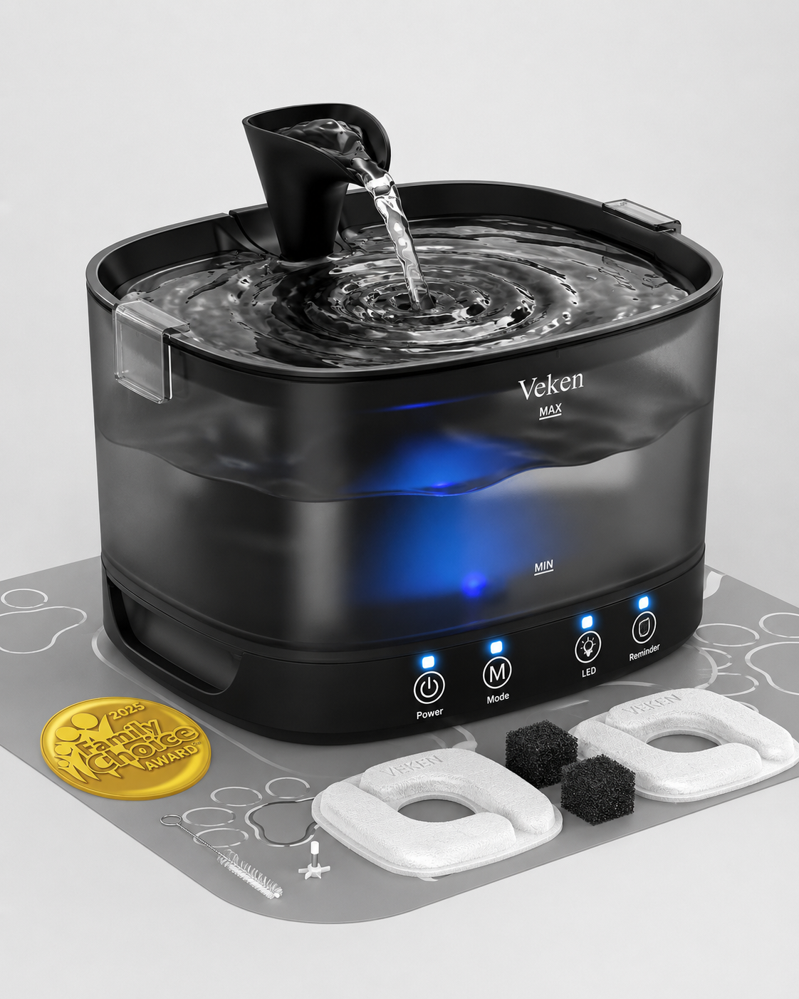 Veken MAX water fountain and humidifier in black, shown with water flowing from the spout, blue internal lighting, and accessories including white and black filter pads and a gold coin on a gray surface.
